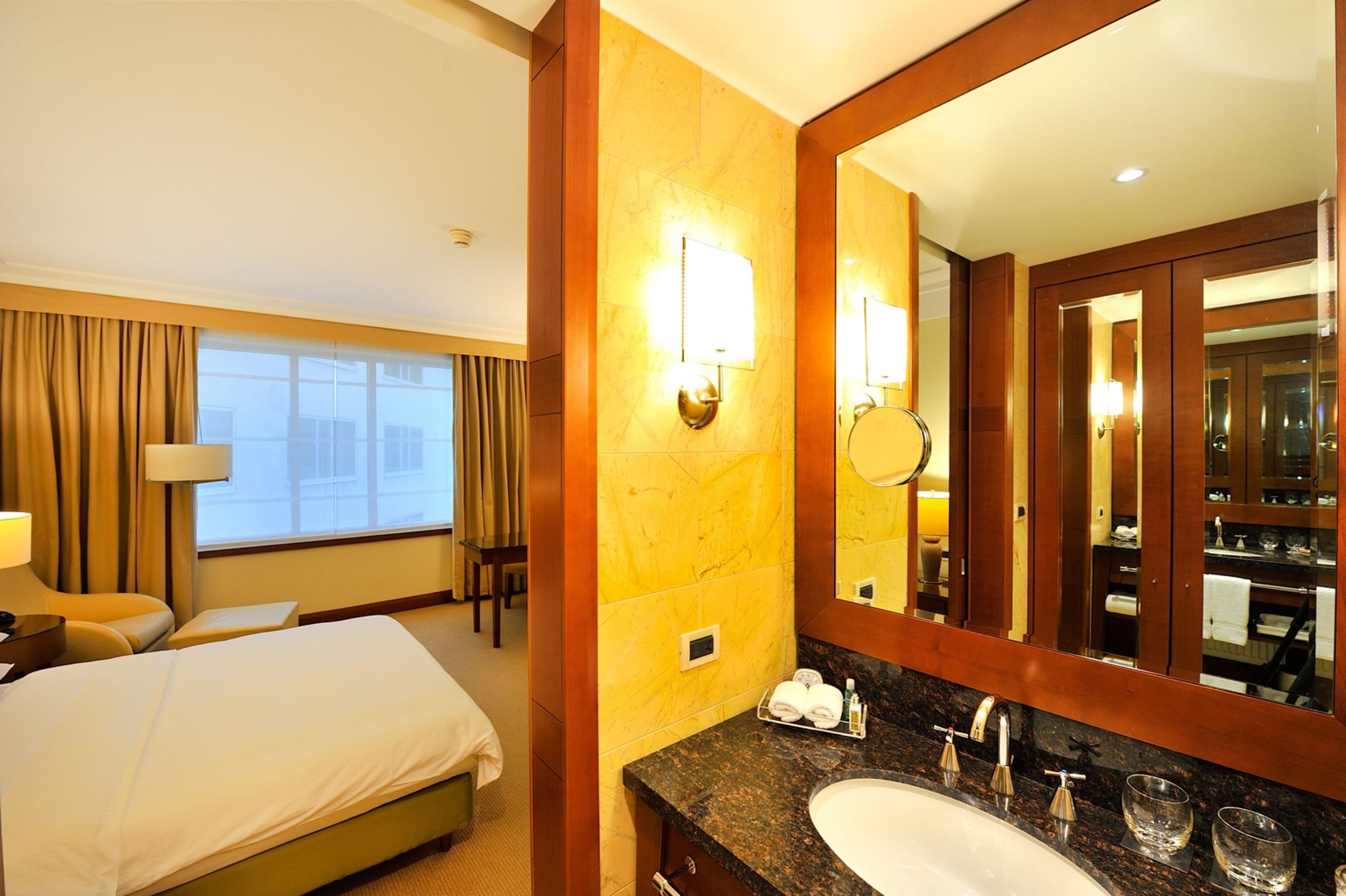A hotel room with a large bed, a bathroom with a sink and mirror, and a window with curtains.