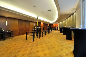 A hotel lobby with a patterned carpet, wooden panel walls, and black tables and chairs.
