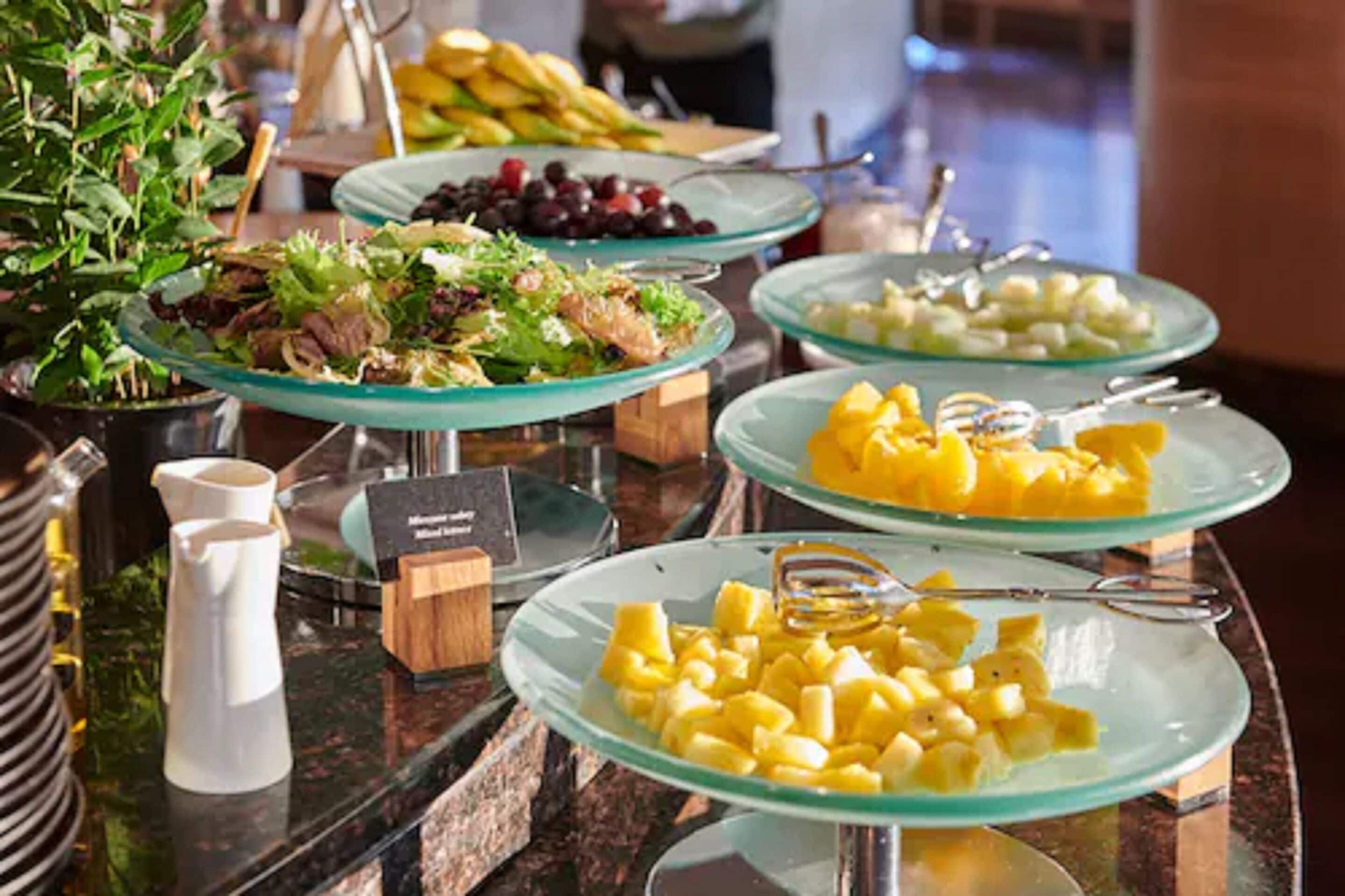 A buffet with various dishes including salads, fruits, and a pitcher.