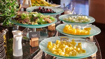 A buffet with various dishes including salads, fruits, and a pitcher.
