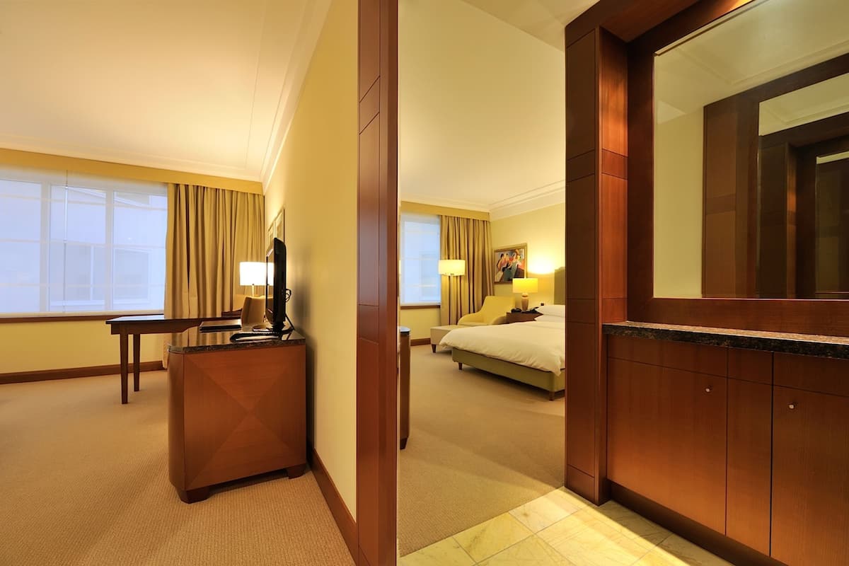 A hotel room with a desk, a bed, a large mirror, and a window with curtains.