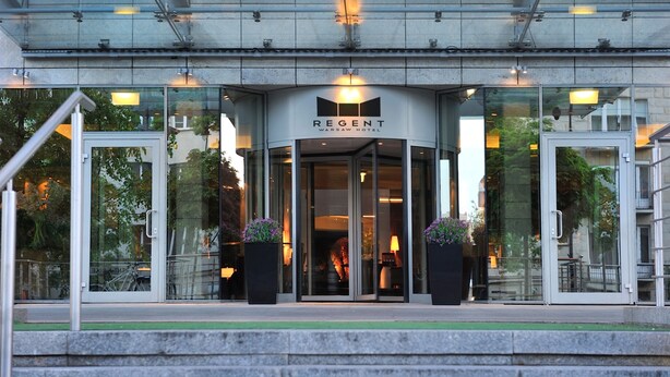 El exterior del Hotel Regent Varsovia, con fachada de vidrio, una entrada moderna y asientos al aire libre visibles a través de las ventanas.