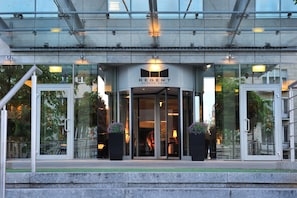 The exterior of the Regent Warsaw Hotel with a glass facade, a modern entrance, and outdoor seating visible through the windows.