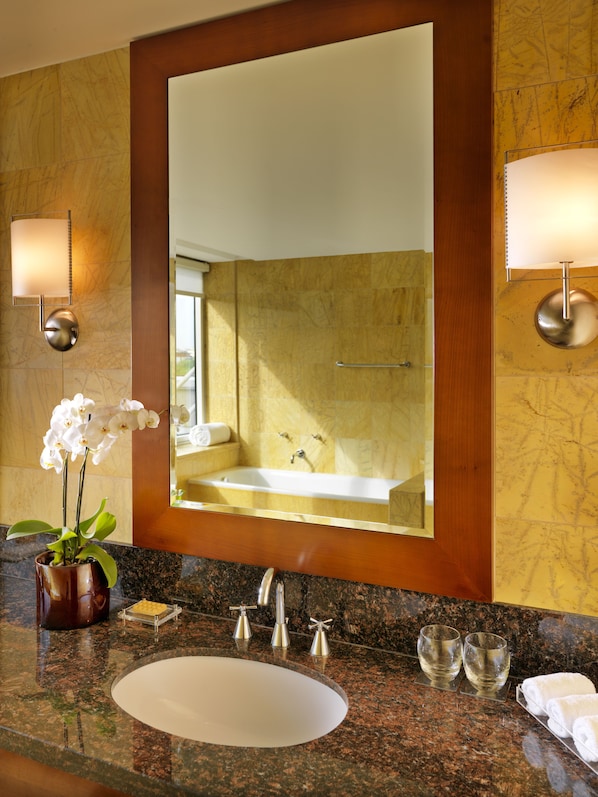 A bathroom with a large mirror, a sink, two wall-mounted lights, a potted orchid, and a towel rack.
