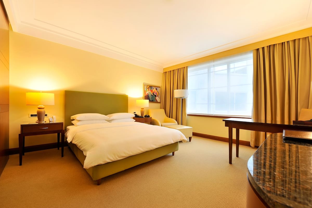 A hotel room with a bed, bedside tables, a desk, a chair, and a window with curtains.