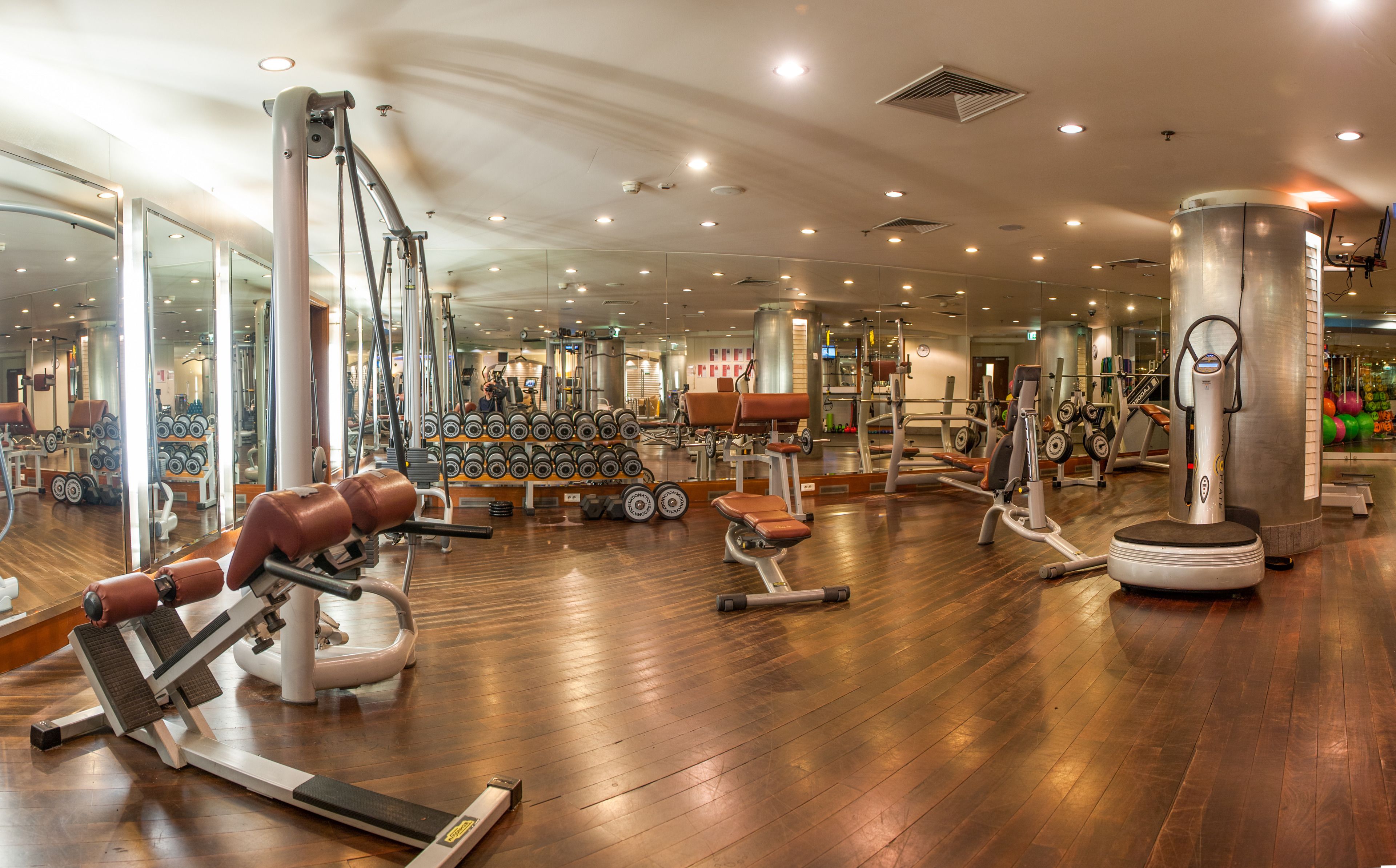 Un gimnasio amplio con diversos equipos de ejercicio, incluyendo cintas de correr, máquinas de pesas y pesas libres.