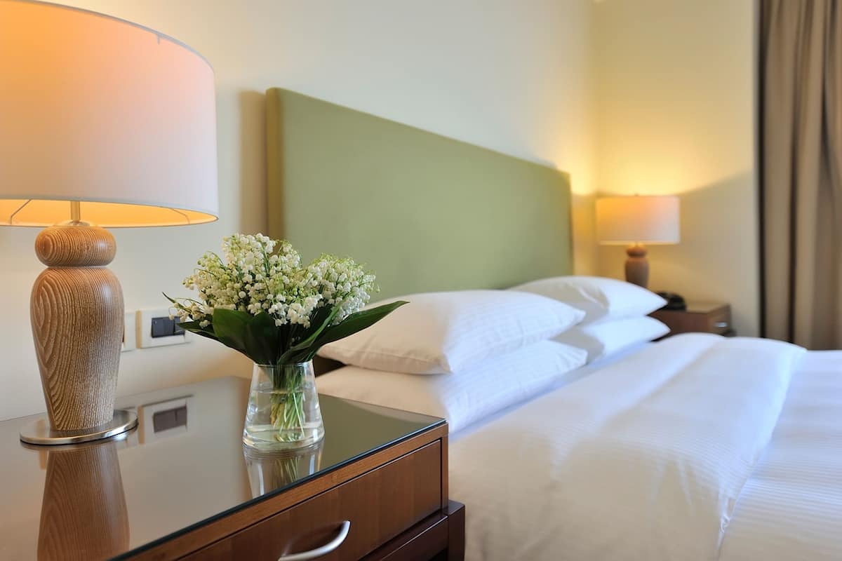 A hotel room with a bed, a nightstand, a lamp, and a vase with flowers.