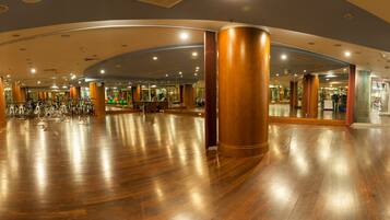 A spacious indoor area with wooden flooring, large cylindrical columns, and various fitness equipment.