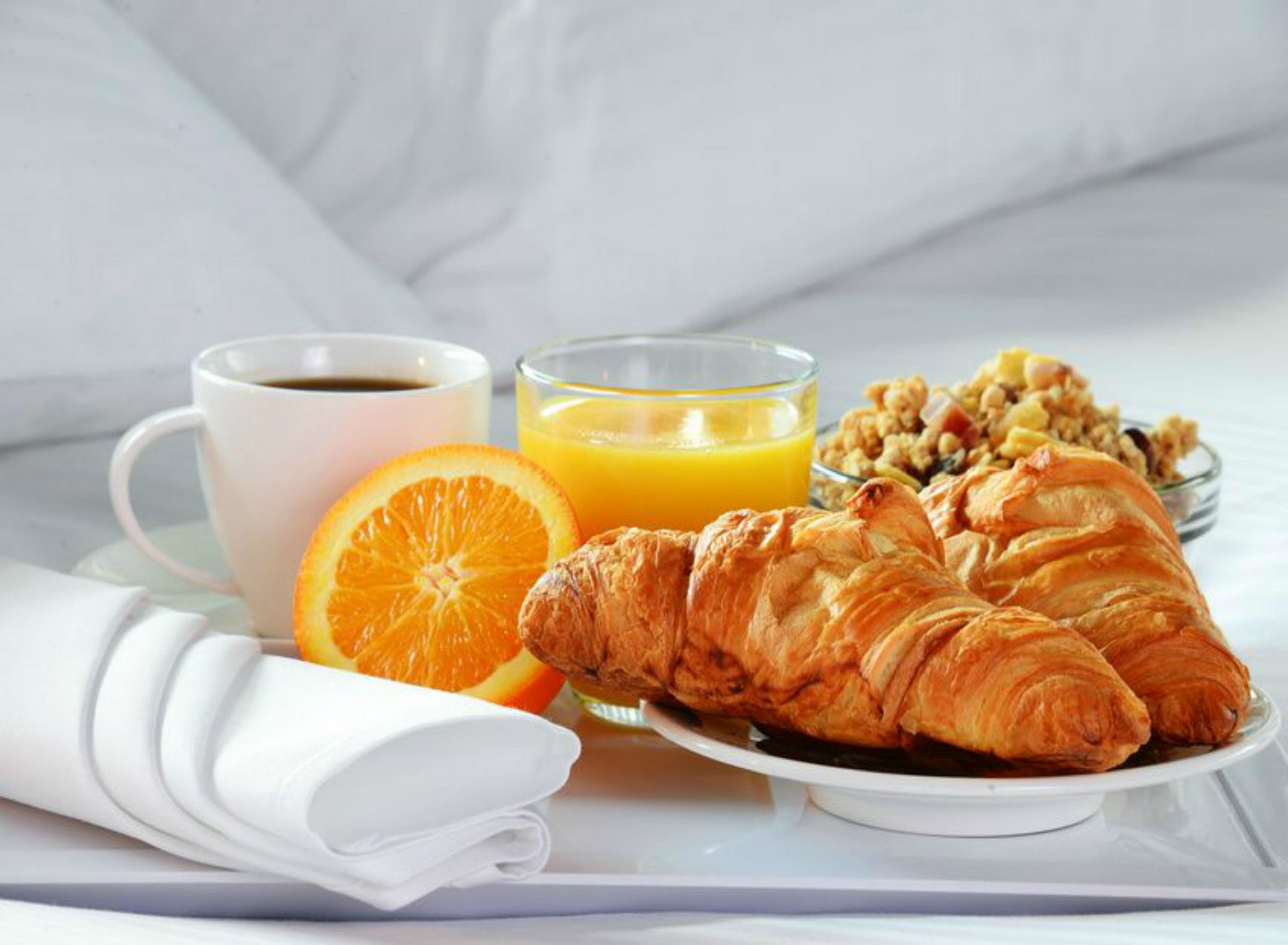 Een ontbijtje met croissants, sinaasappelsap, koffie en een schaal met noten op een dienblad.