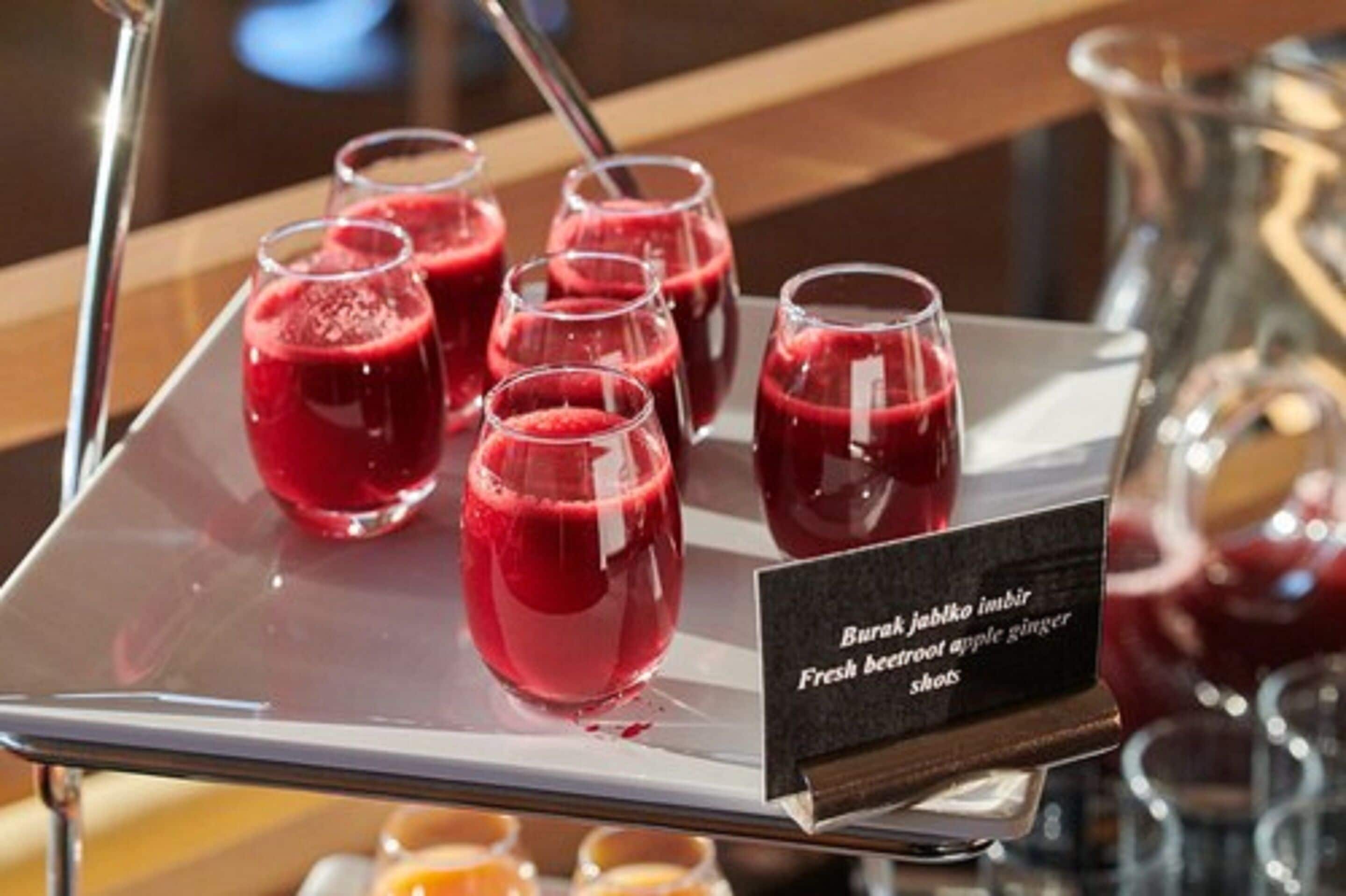 A tray with several glasses of red beverage, a sign indicating 'Burrak jublo imbir' and 'Fresh beetroot apple ginger shots'.