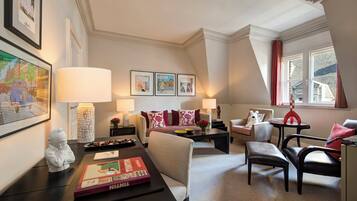 A well-lit living room with a sofa, armchairs, a coffee table, and a dining table with a book and a lamp.