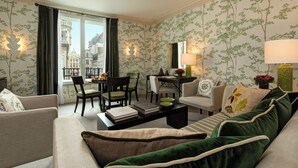 Una habitación de hotel moderna con comedor, sofá, mesita de centro y vistas a un edificio histórico a través de la ventana.