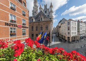 A hotel with a brick facade, a large window with red flowers, and a view of a historic building with a tower.