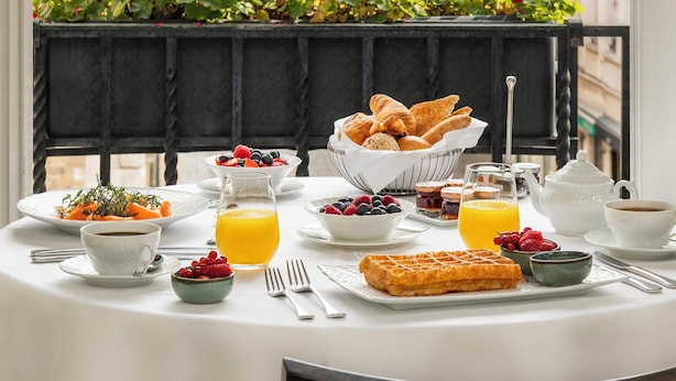 Una mesa de desayuno con diversas comidas y una maceta con flores rojas.