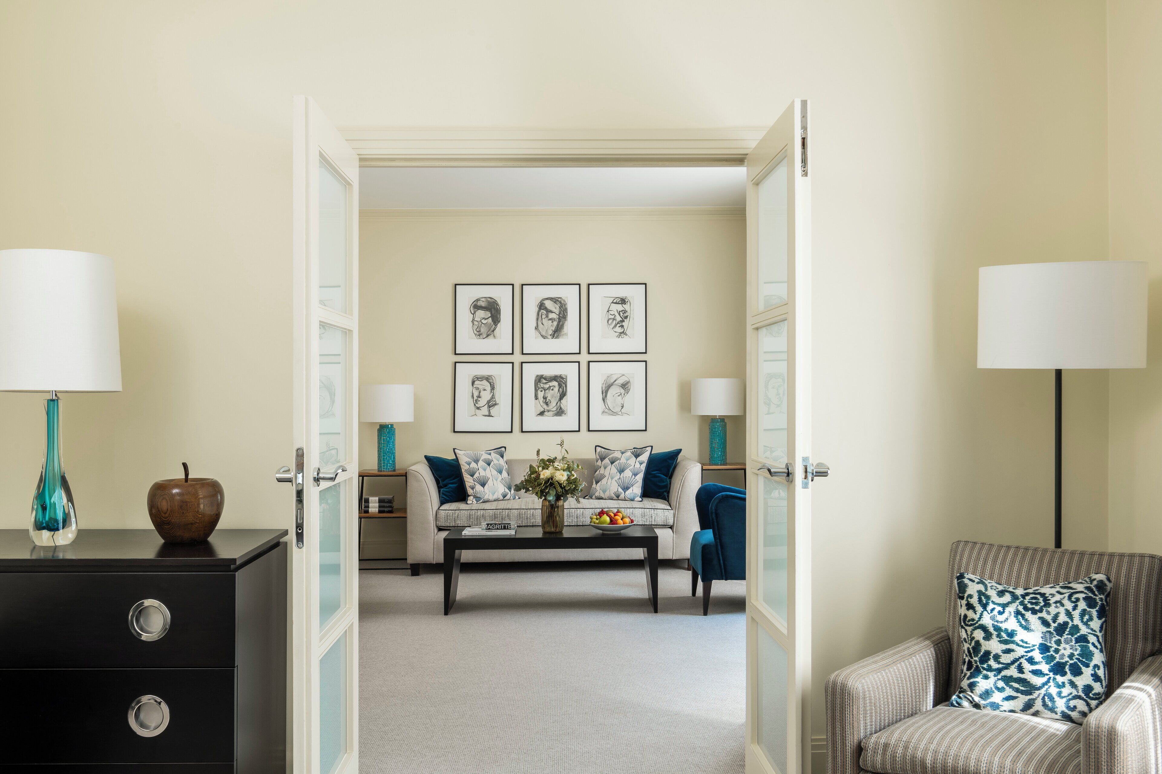 A living room with a sofa, coffee table, and armchairs. There are framed pictures on the wall and a vase with flowers on the coffee table.