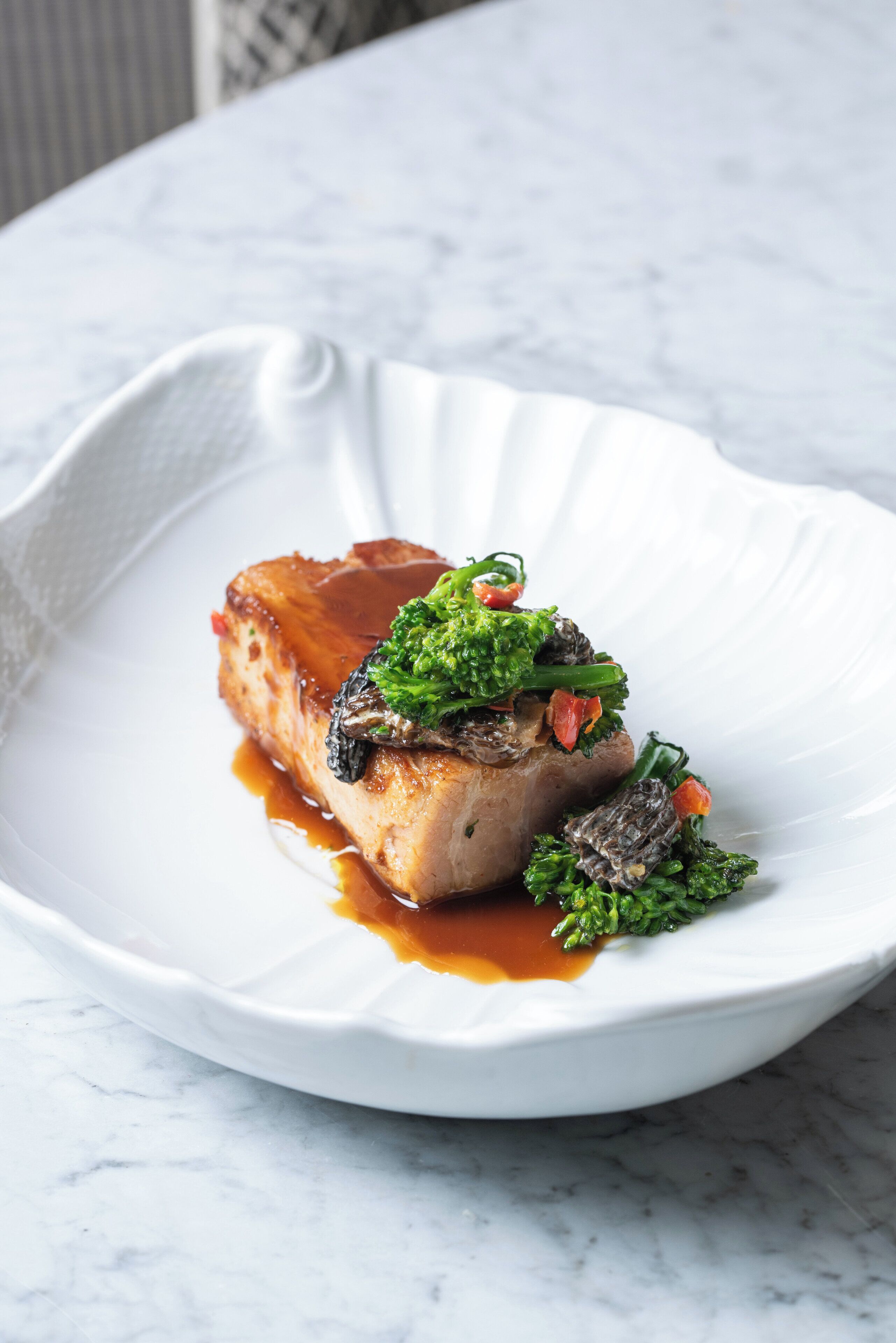 Un plato blanco con carne y verduras sobre una superficie de mármol.