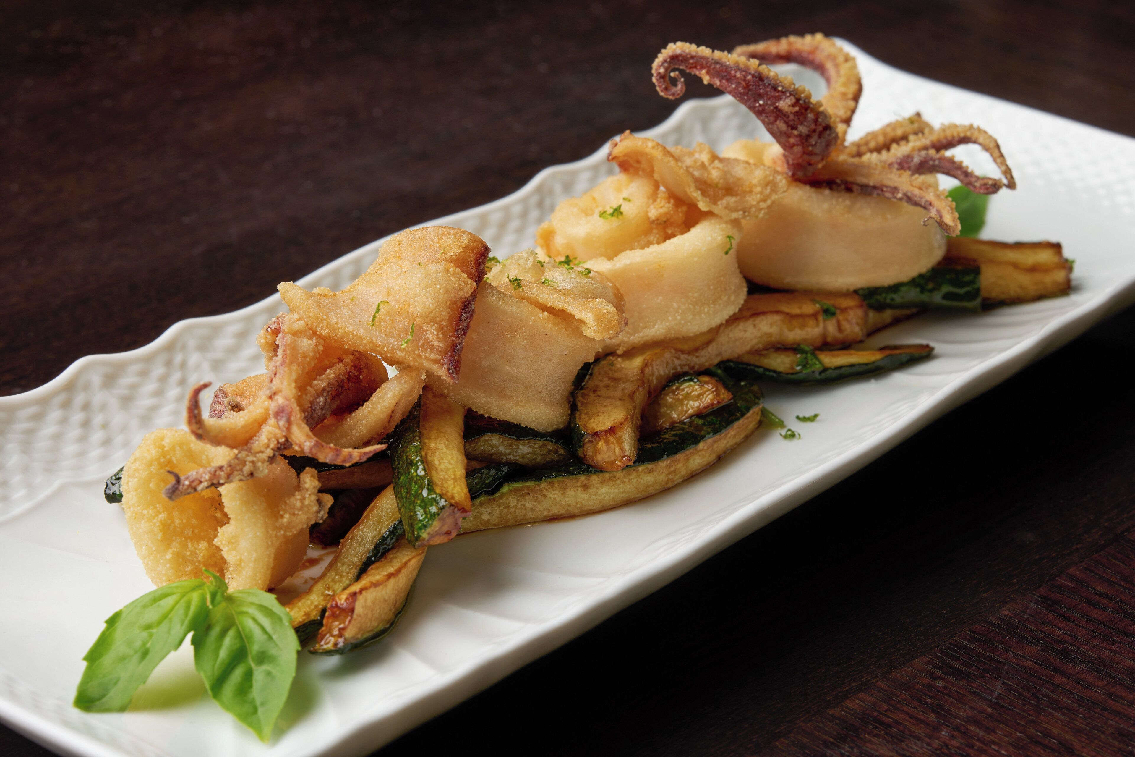 A plate of food with fried squid, potatoes, and greens, garnished with basil.
