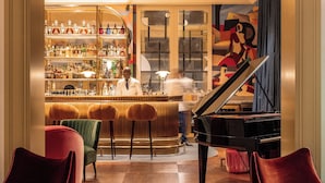 Zona de bar con piano, taburetes y un cantinero.