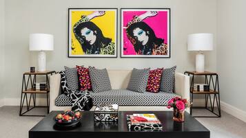 Ein Wohnzimmer mit einer Couch, zwei Beistelltischen, einem Couchtisch mit Büchern und einer Obstschale, sowie zwei gerahmten Kunstwerken an der Wand.