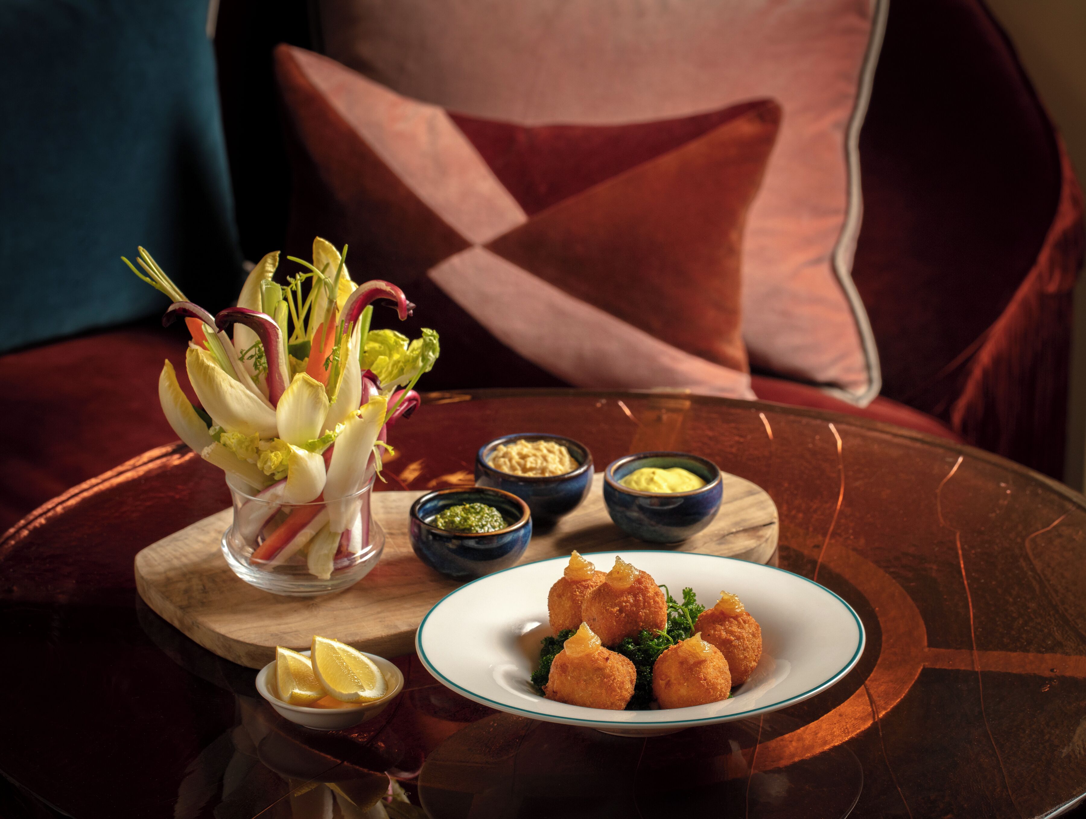A dining table with a plate of croquettes, a bowl of salad, and two small bowls of condiments.