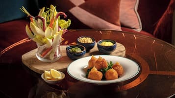A dining table with a plate of croquettes, a bowl of salad, and two small bowls of condiments.