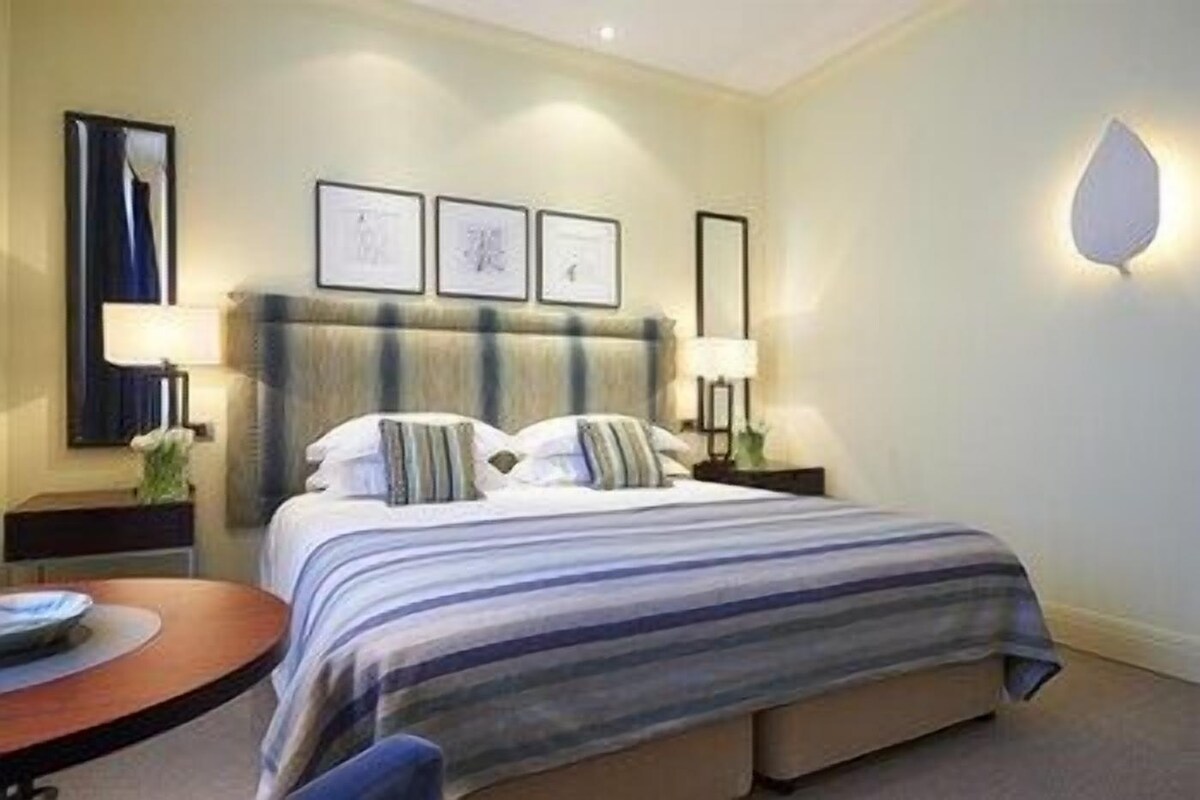 Una habitación de hotel con cama, mesitas de noche, lámparas y cuadros en la pared.