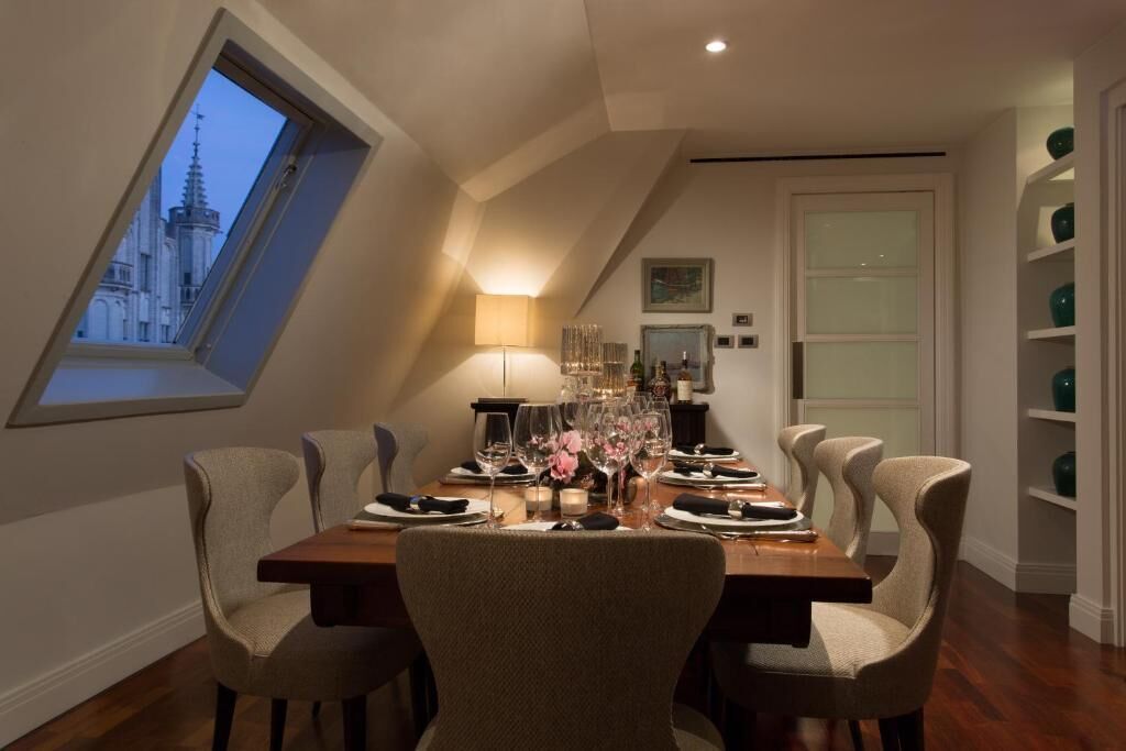 A dining room with a high ceiling and a skylight, a table set for six, and a view of a building through the skylight.