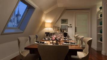 A dining room with a high ceiling and a skylight, a table set for six, and a view of a building through the skylight.