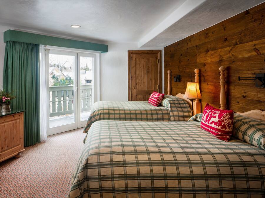 A bedroom with two beds, a wooden headboard, a nightstand with a lamp, and a view through a glass door.