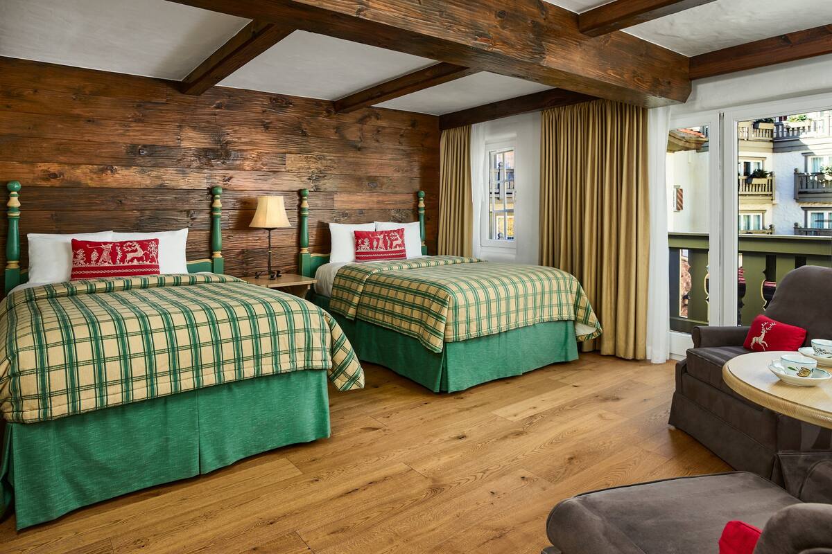 A room with two beds, wooden flooring, and a view of a balcony.