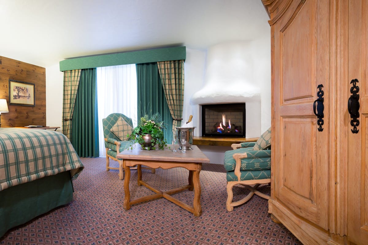 A hotel room with a bed, a table, a chair, a fireplace, and a wardrobe.