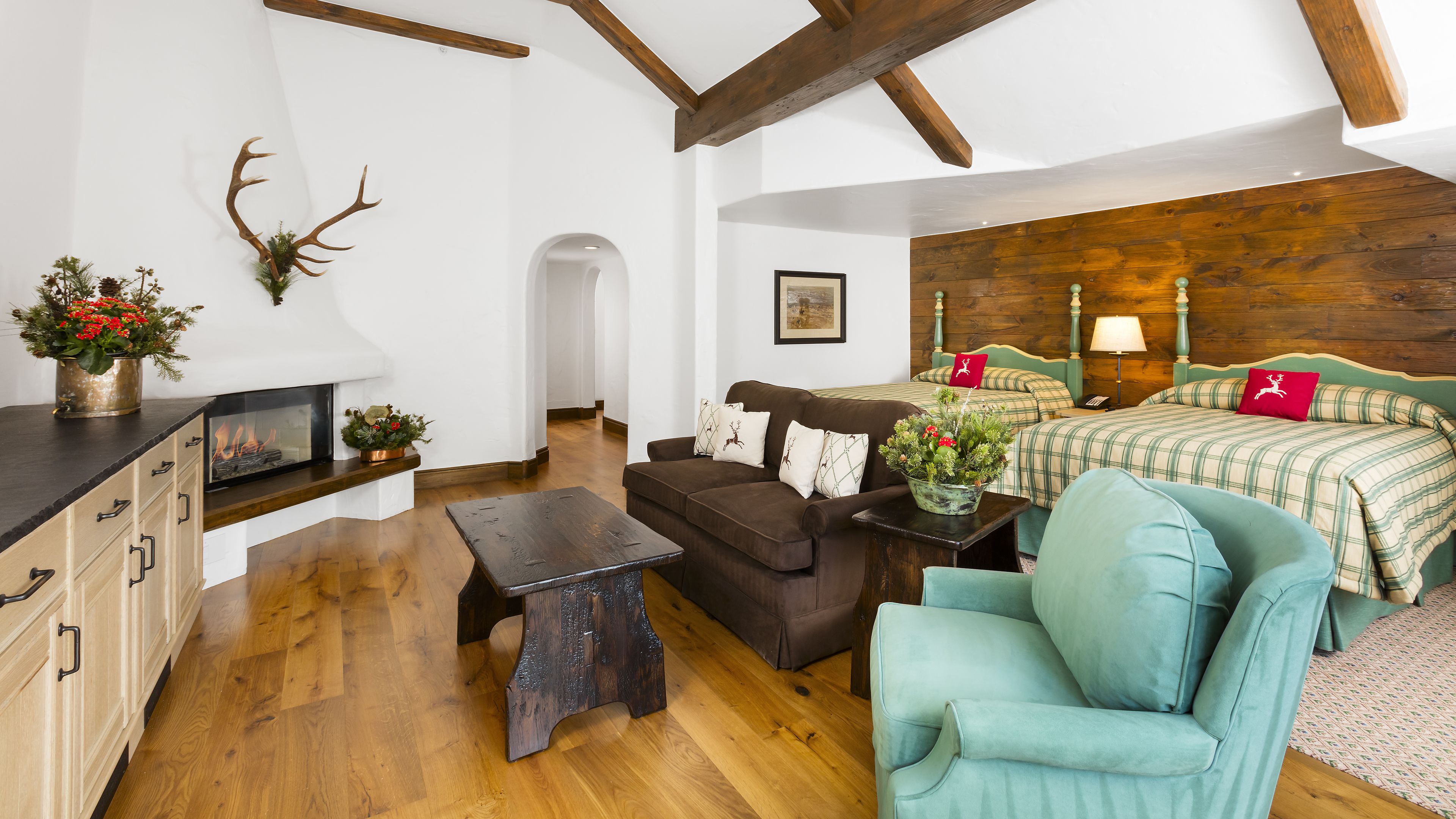A cozy room with a fireplace, wooden beams, a bed with plaid bedding, and a teal armchair.