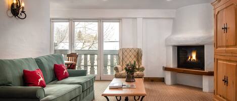 A living room with a green sofa, a wooden coffee table, a fireplace, and a large window.
