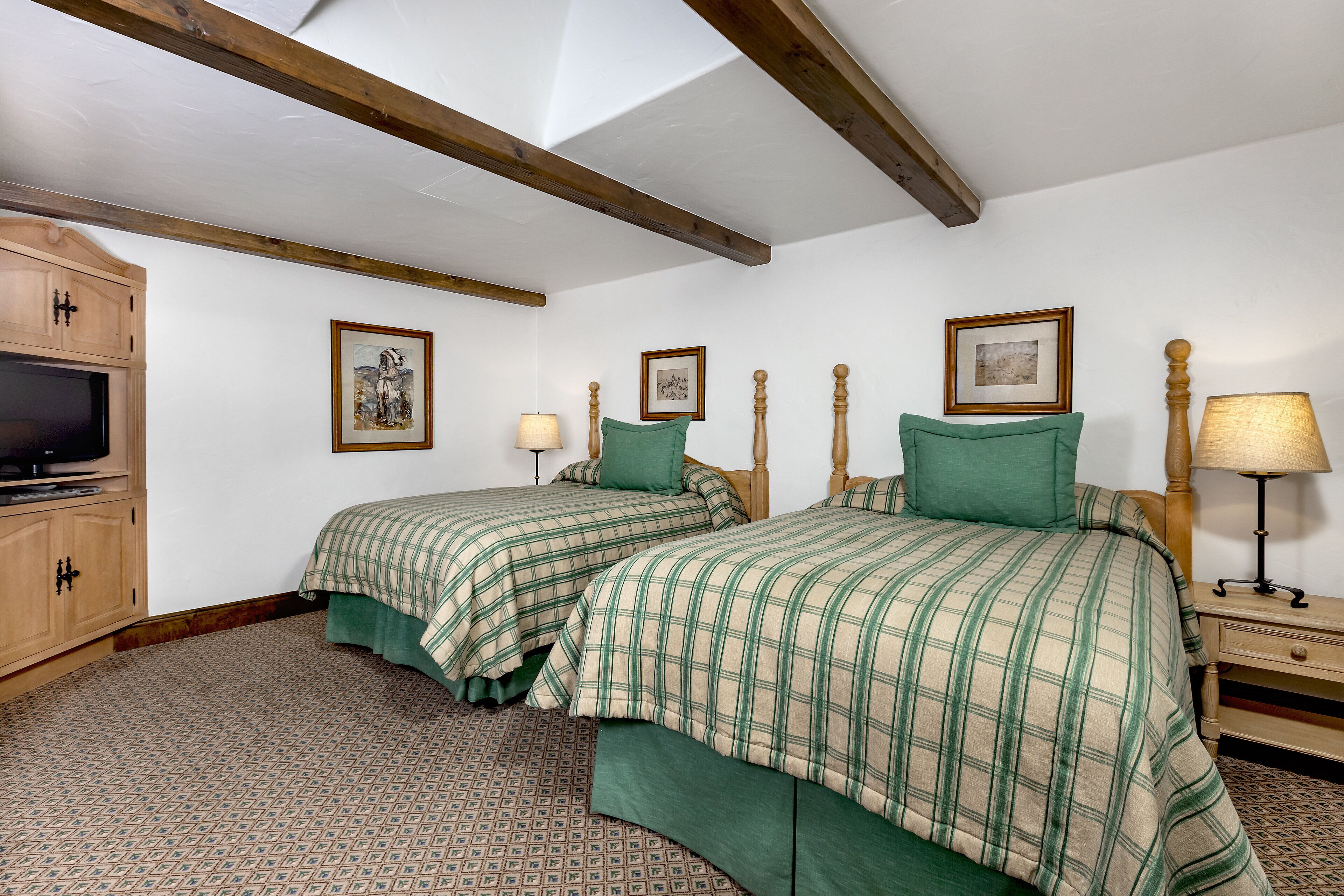 A bedroom with two beds, wooden headboards, a TV, and framed pictures on the wall.