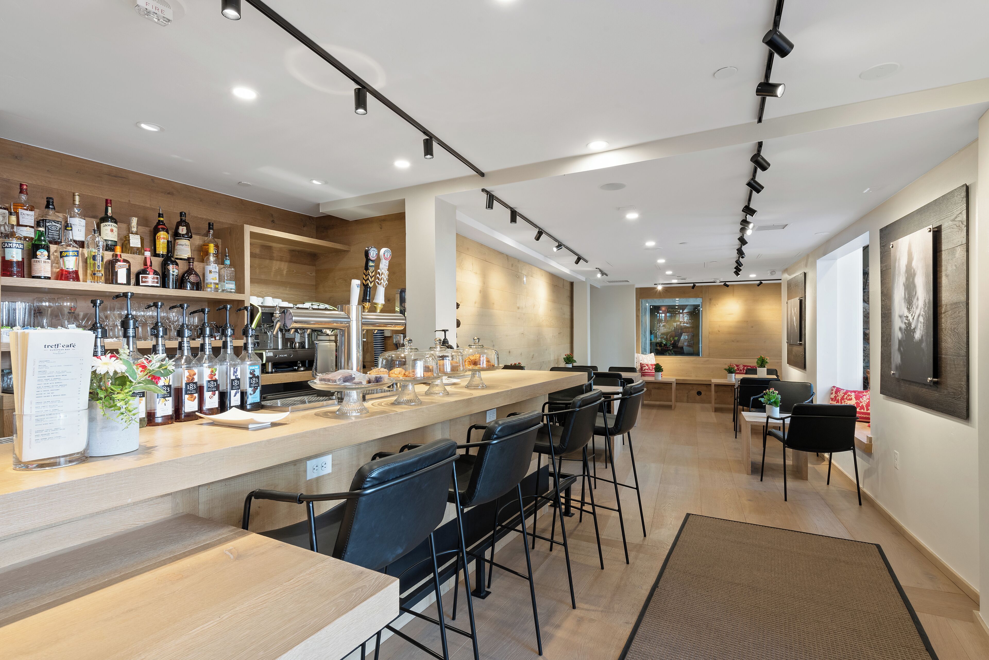 A bar area with a long counter, multiple stools, and a variety of liquor bottles.