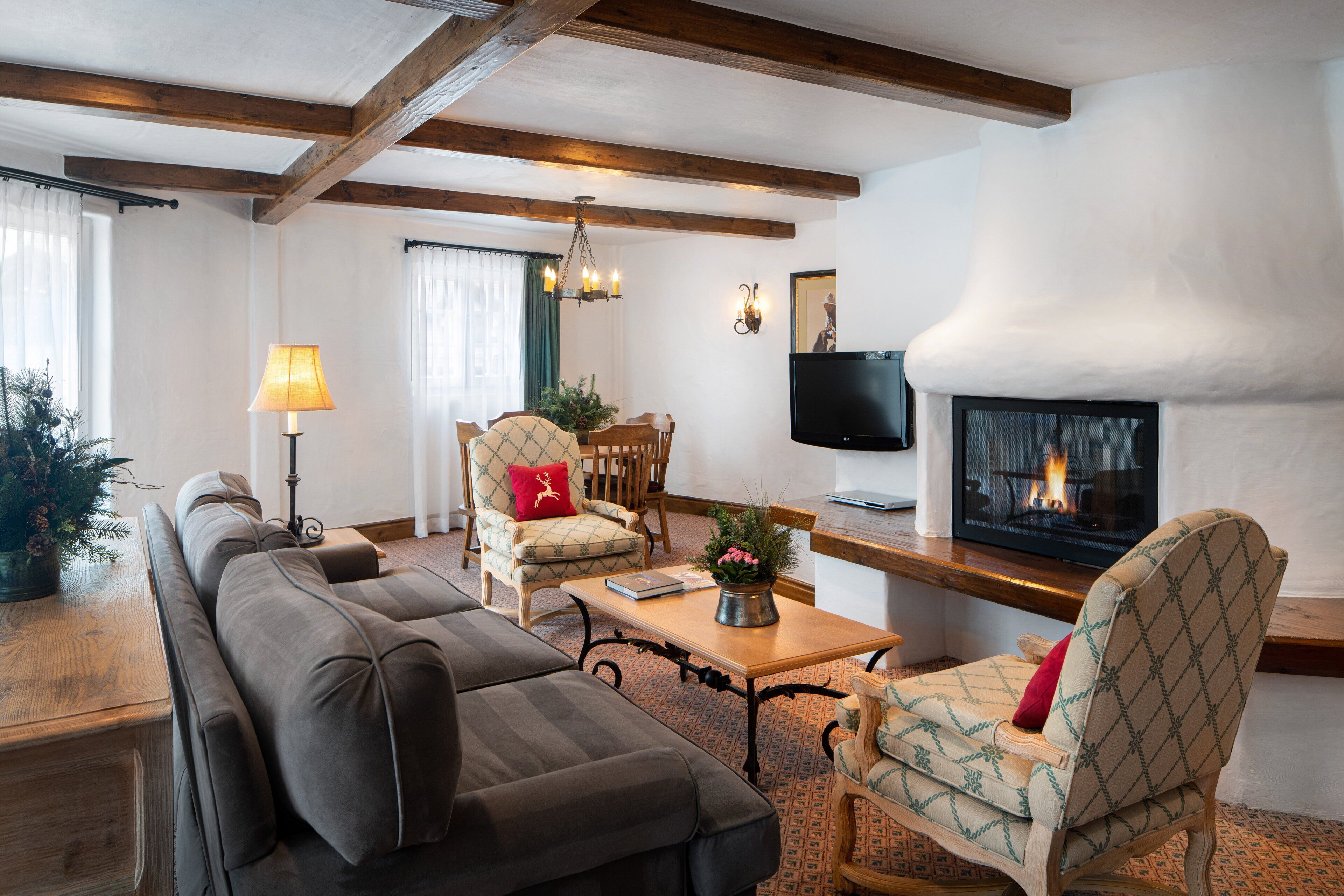 A cozy living room with a fireplace, wooden beams, a sofa, chairs, and a television.