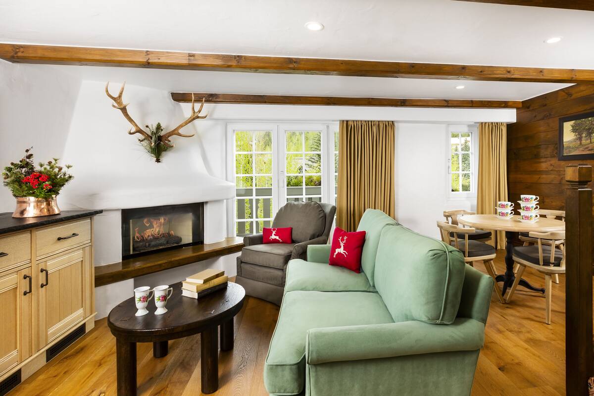 A cozy living room with a fireplace, a green sofa, a wooden staircase, and a dining area with a table set for four.