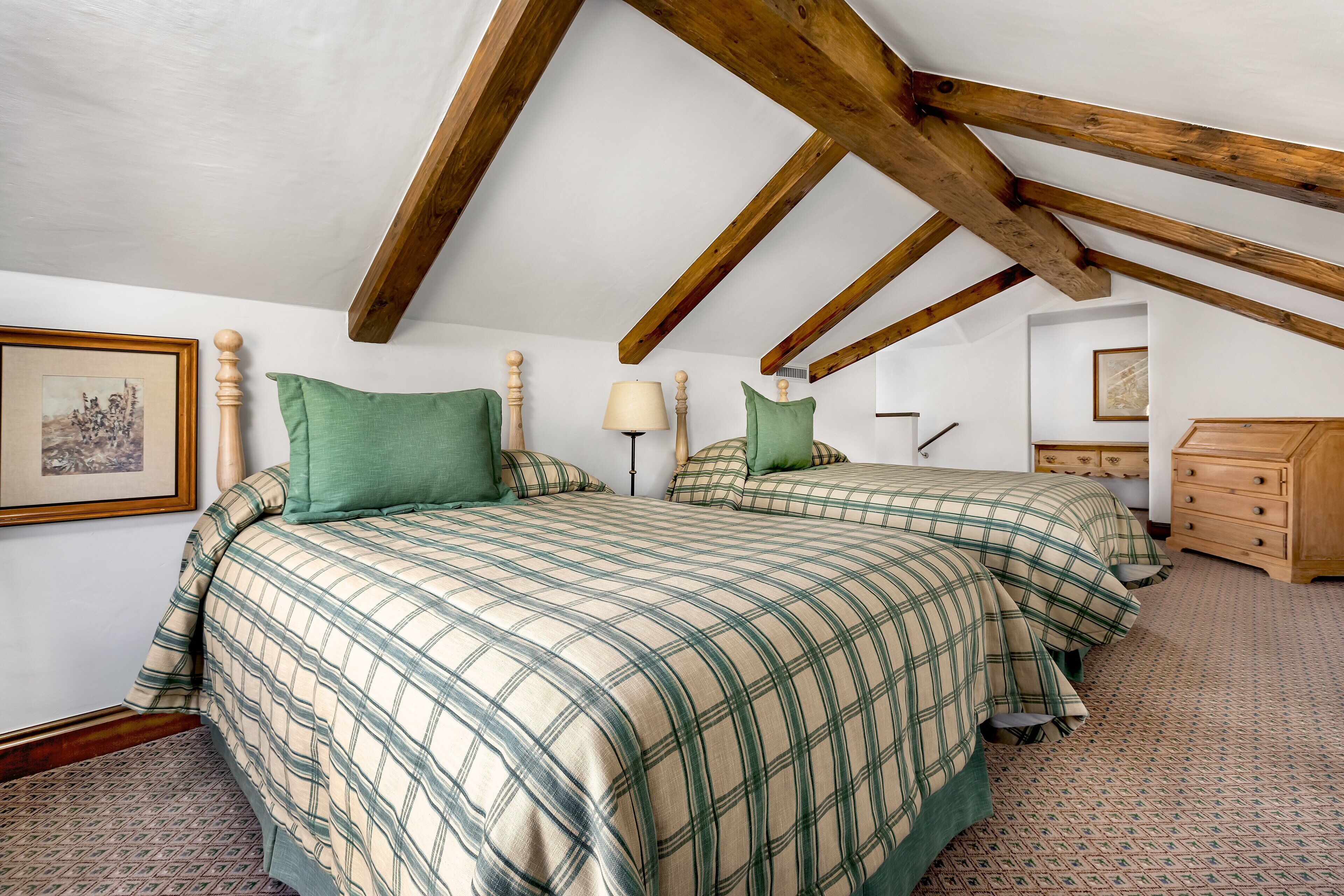 A bedroom with two beds, wooden beams on the ceiling, a dresser, and a framed picture on the wall.