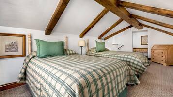 A bedroom with two beds, wooden beams on the ceiling, a dresser, and a framed picture on the wall.