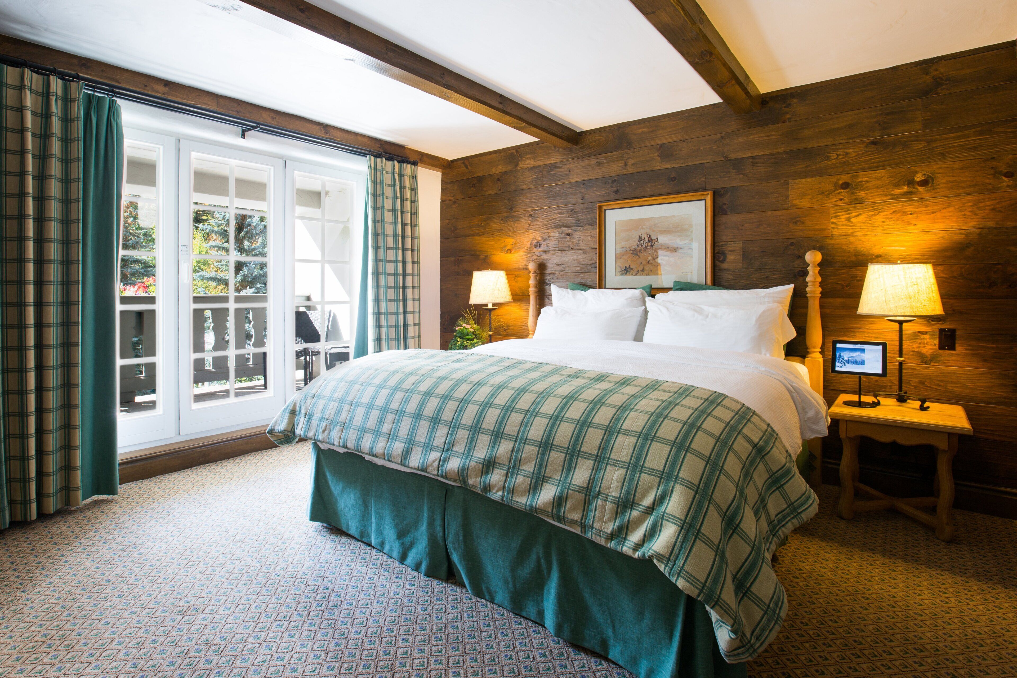 A bedroom with a large bed, two bedside tables with lamps, a wooden wall, and a window with curtains.