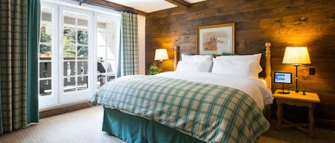 A bedroom with a large bed, two bedside tables with lamps, a wooden wall, and a window with curtains.