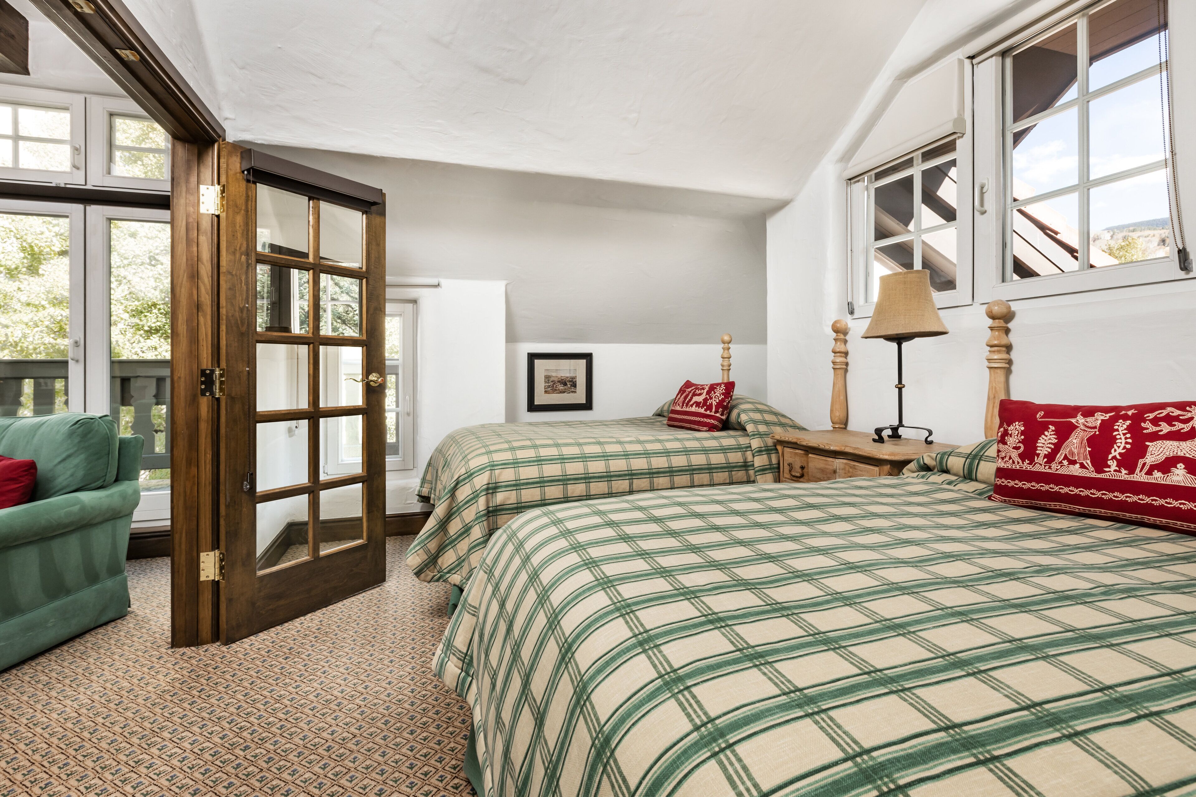 Un dormitorio con dos camas, un sofá verde, una mesita de noche de madera, una lámpara y una puerta que da al exterior.