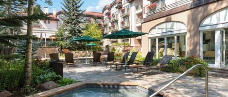 A pool area with lounge chairs and umbrellas, surrounded by greenery and a building with balconies.