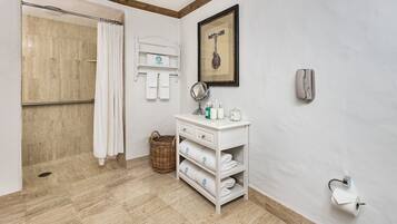 A bathroom with a shower, a vanity with toiletries, and a framed picture on the wall.