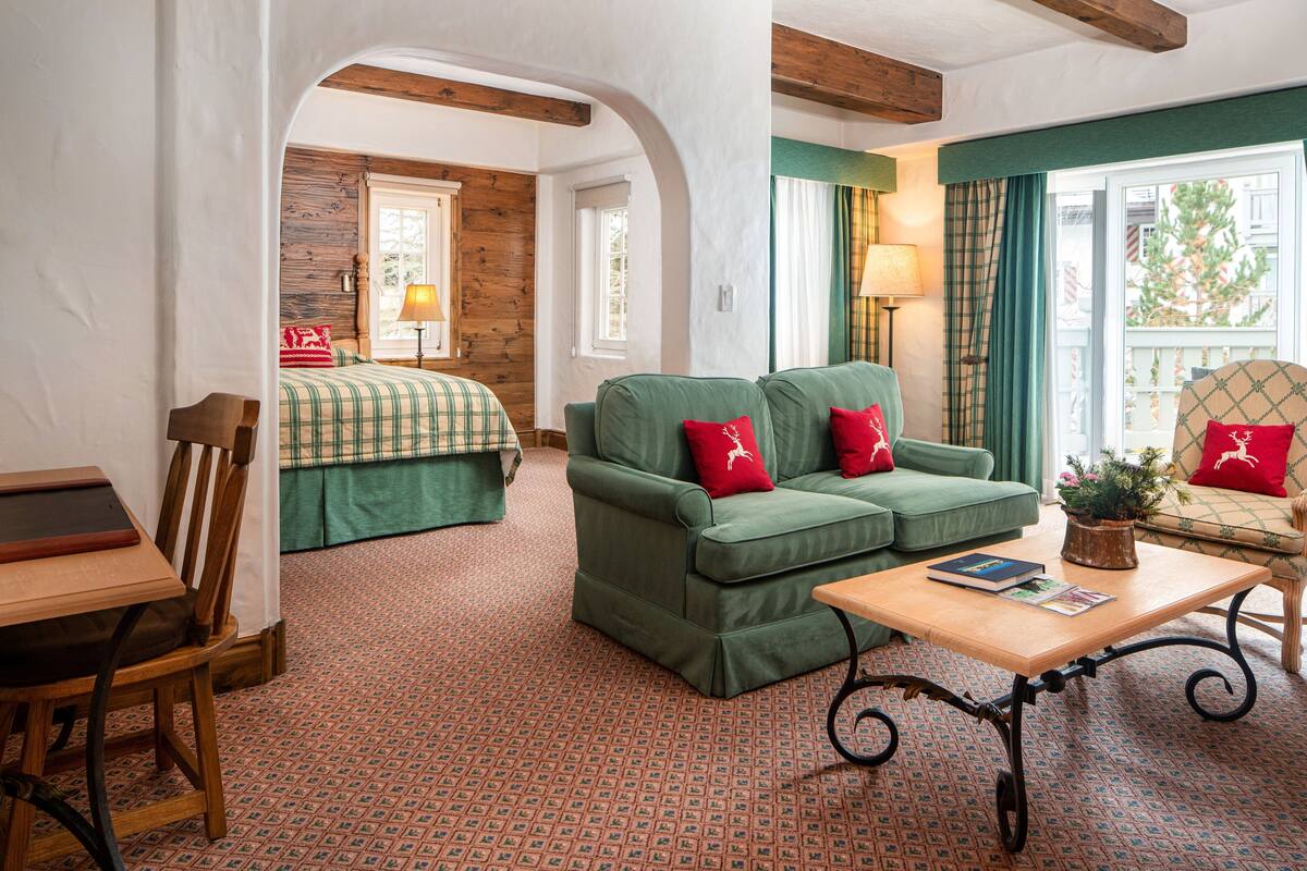 A cozy room with a green sofa, a wooden table, and a bed with plaid bedding.