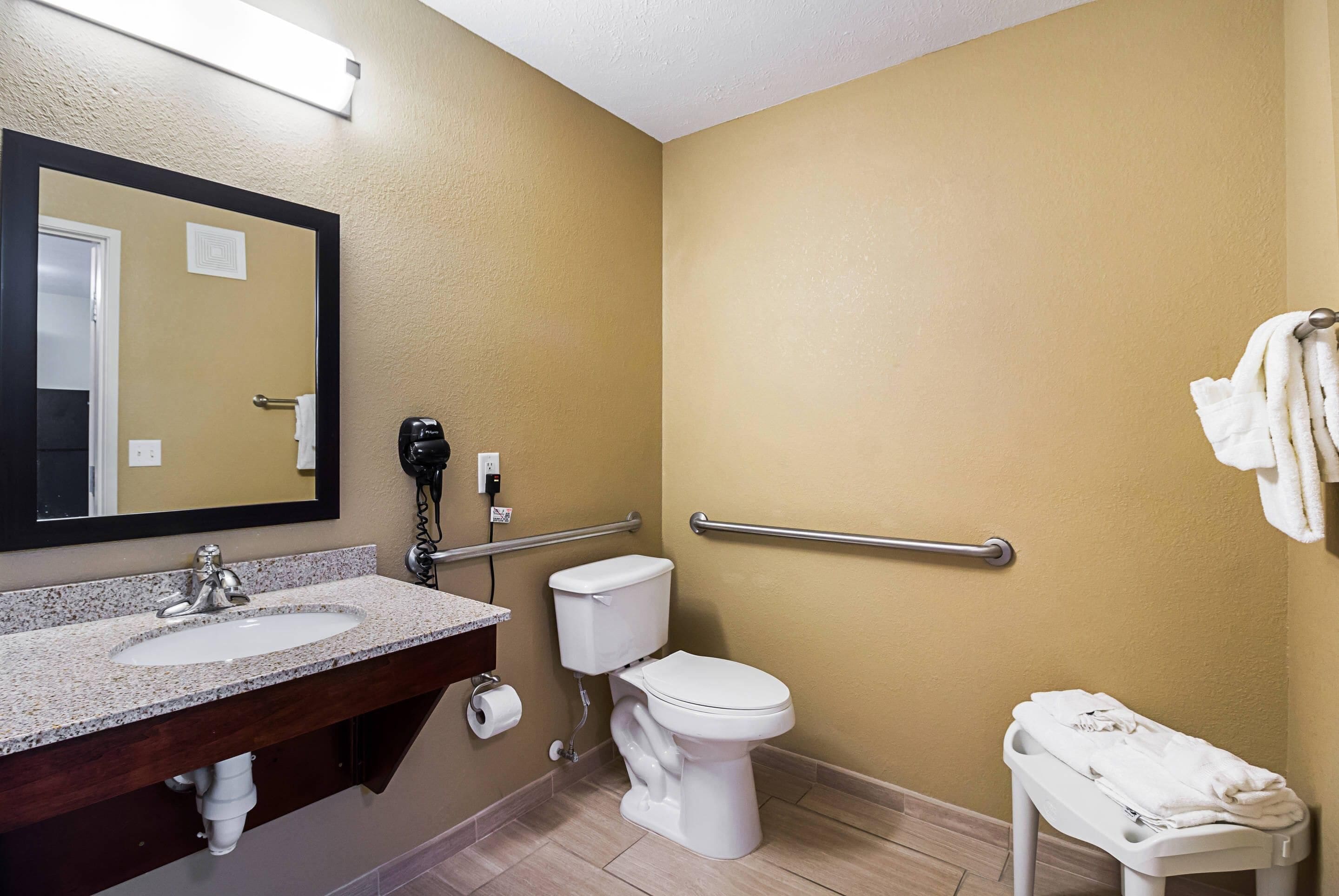 A bathroom with a sink, toilet, and handrails.