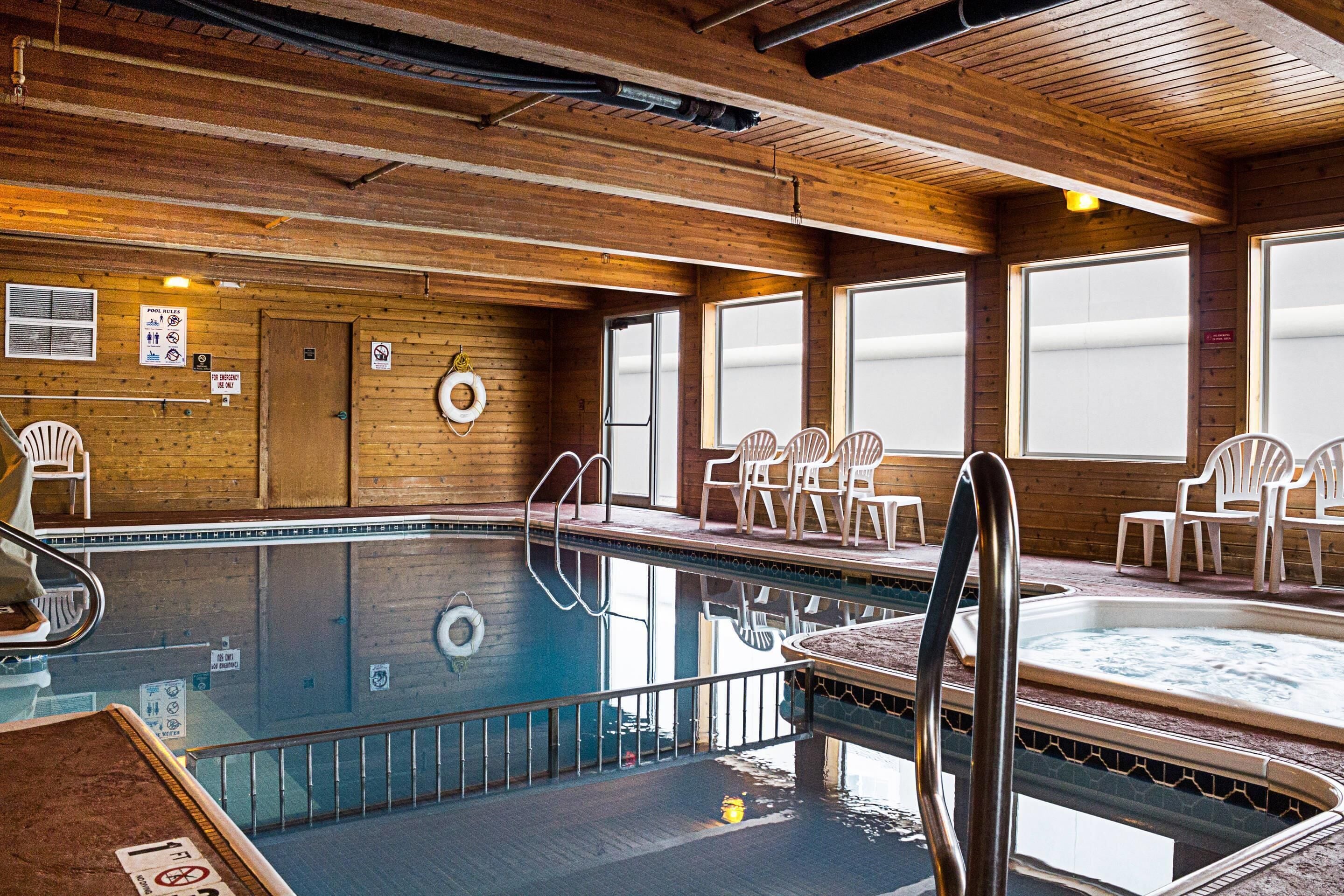 A wooden interior with a pool, chairs, and a hot tub.