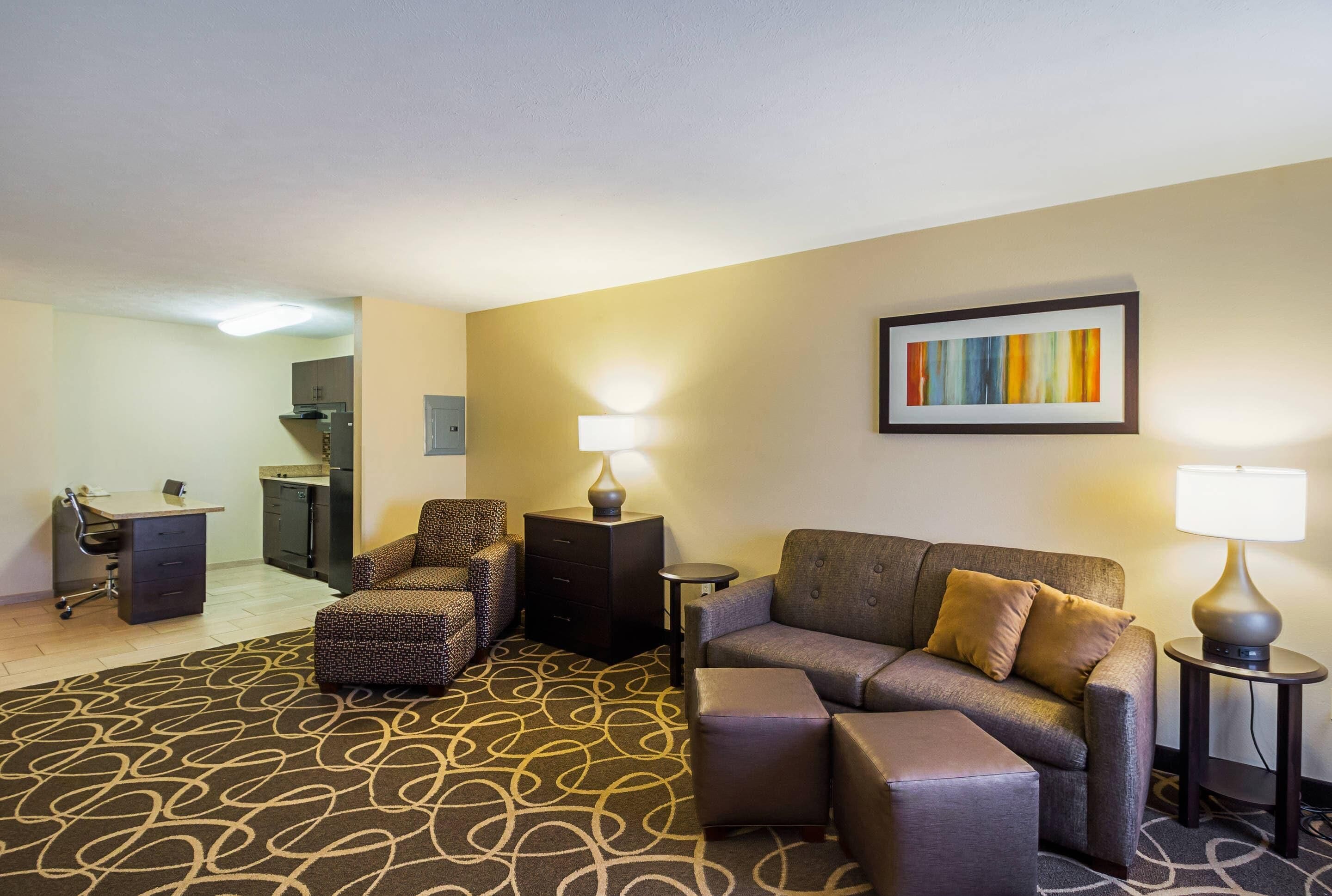 A hotel room with a sofa, armchair, ottoman, desk, and lamp.