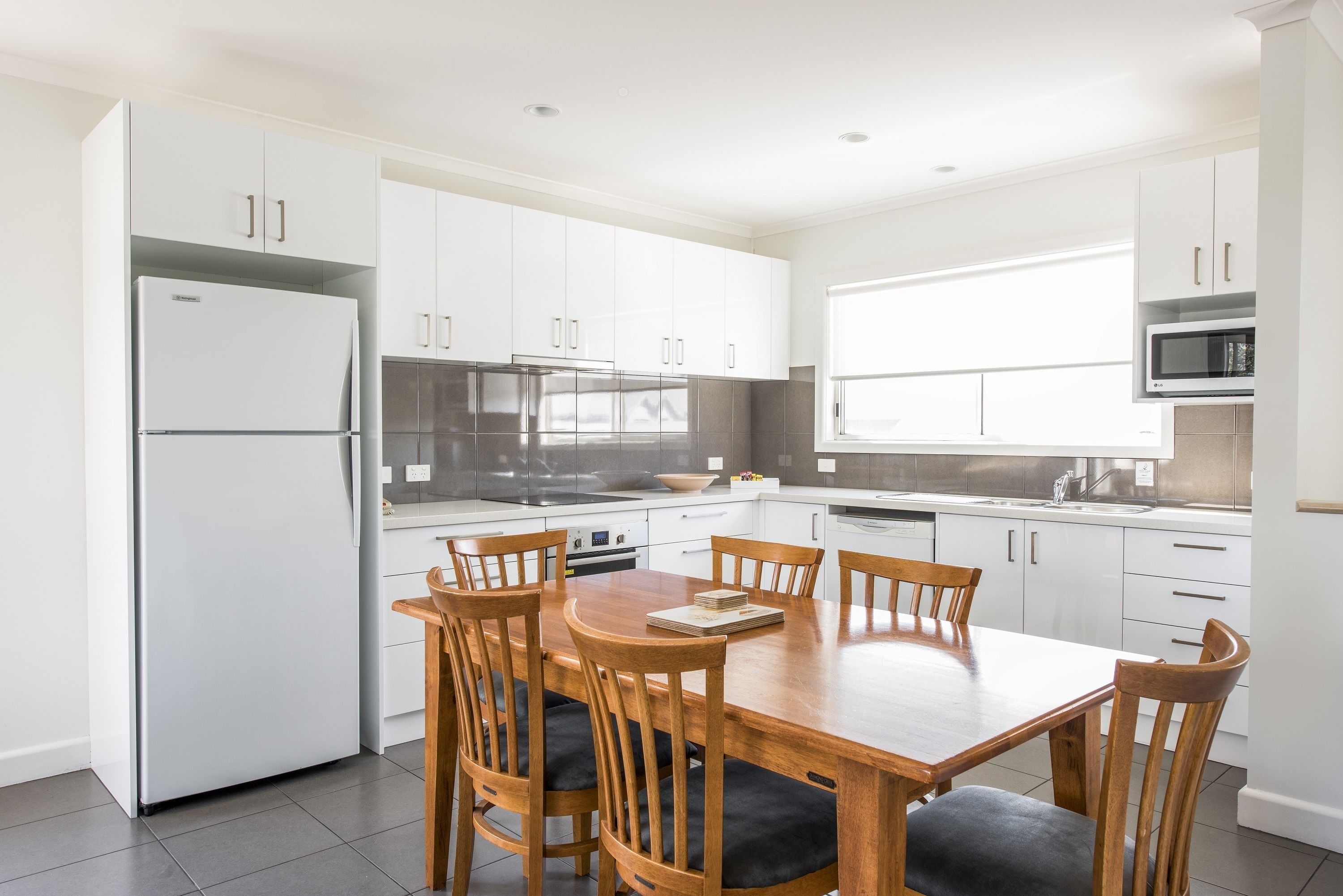 A modern kitchen with white cabinets, a stainless steel refrigerator, a microwave, and a dining table with wooden chairs.