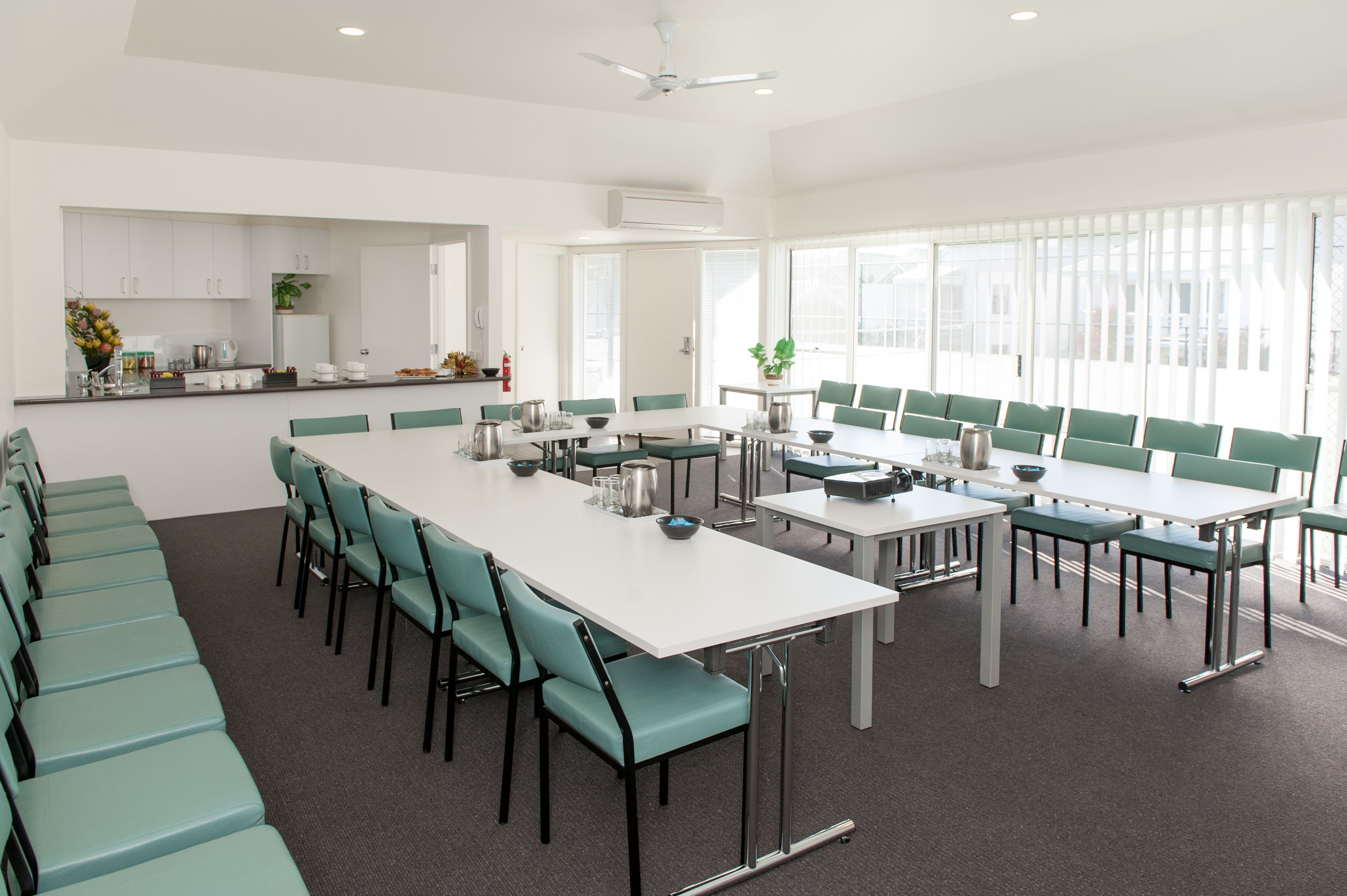 A modern conference room with a long table, green chairs, and a kitchen area in the background.